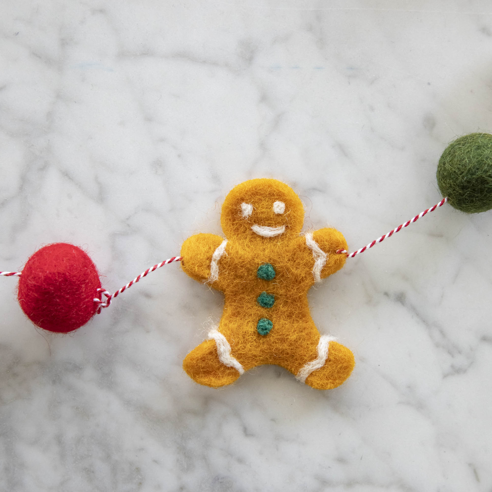 Close up of the Gingerbread Felt Garland showing the gingerbread man and red and green poms on a candy stripe string.