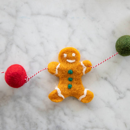 Close up of the Gingerbread Felt Garland showing the gingerbread man and red and green poms on a candy stripe string.