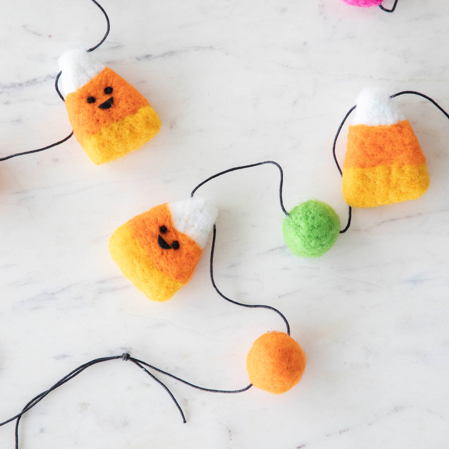 Wool smiley candy corn pieces with a green ball on a string.