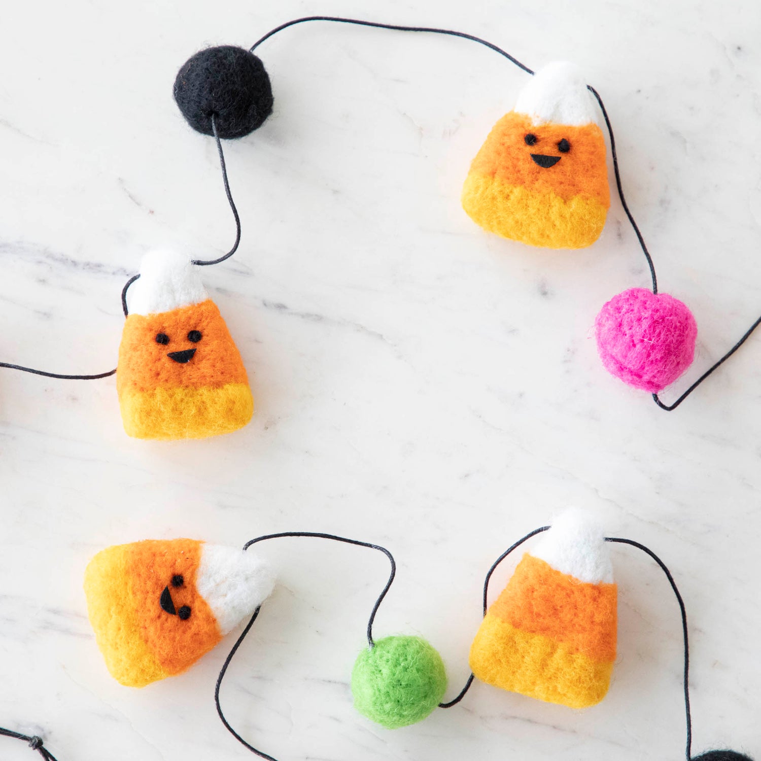 Wool smiley candy corn pieces with colorful balls on a string.