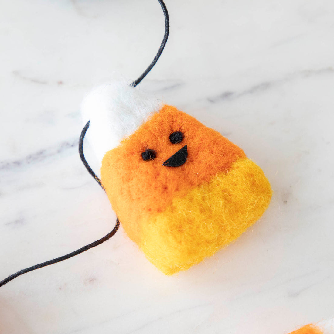 Wool smiling candy corn piece on a black string on a marble table.