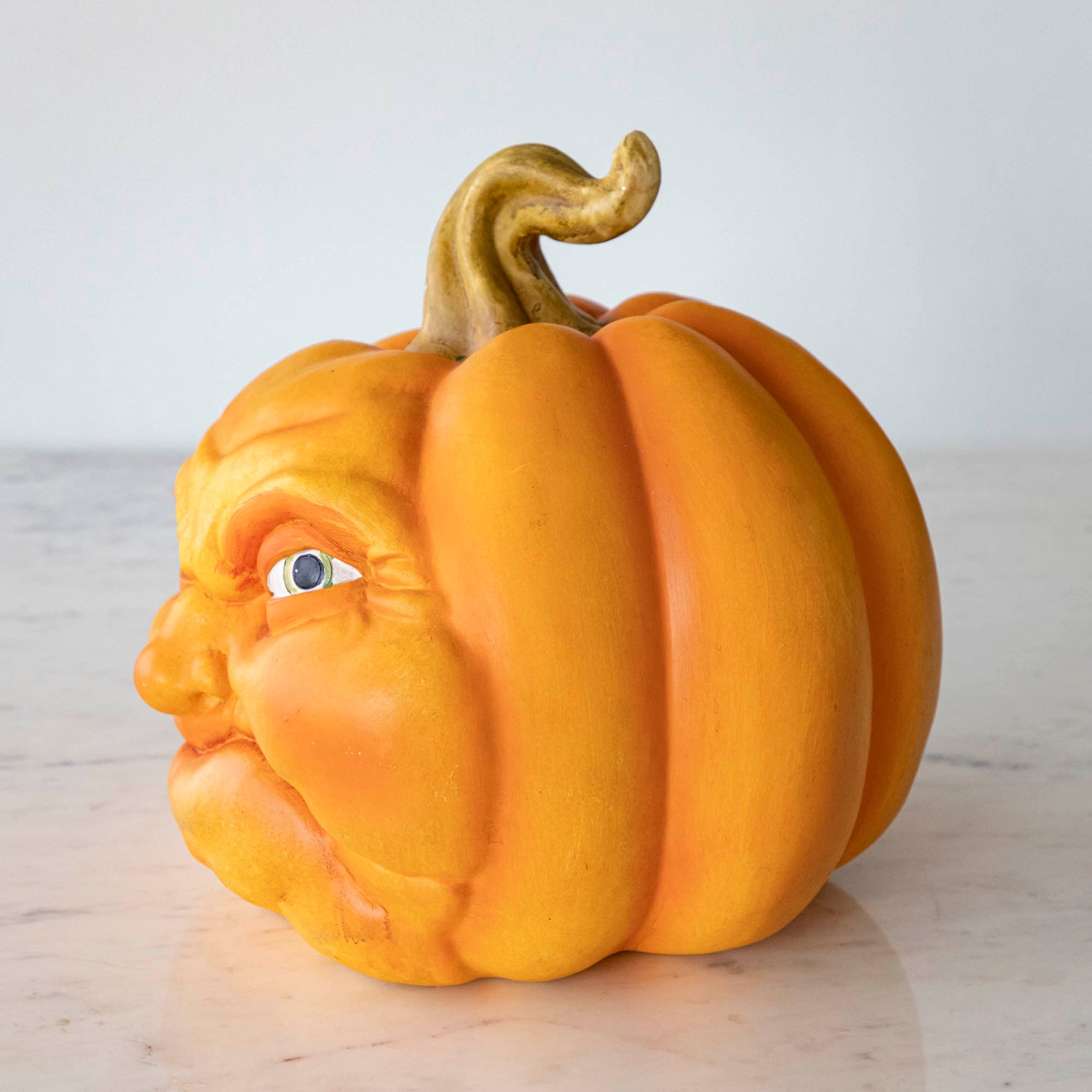 A side-view of a scowling resin pumpkin on a marble table.