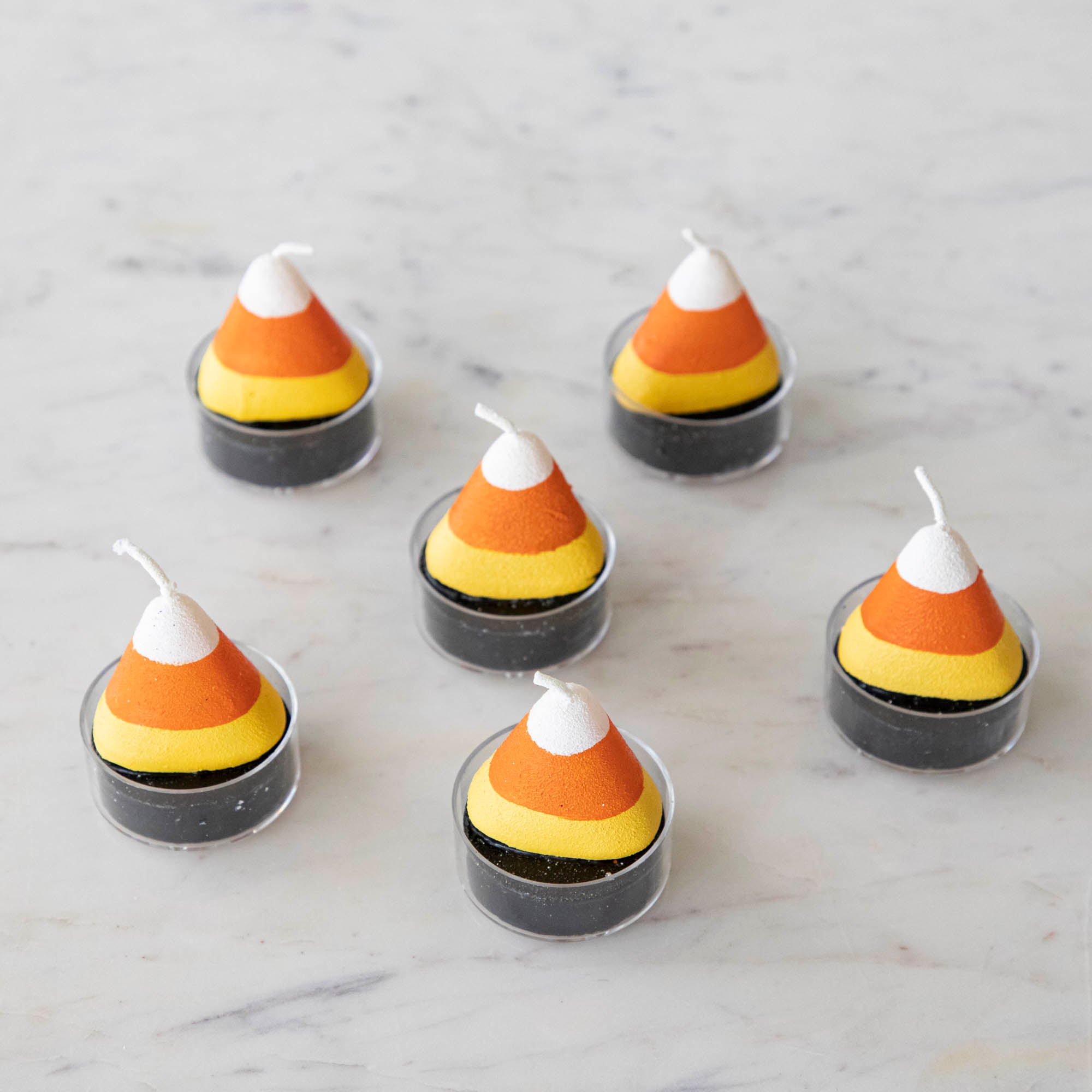 Candy corn themed tea light candles on a marble table.