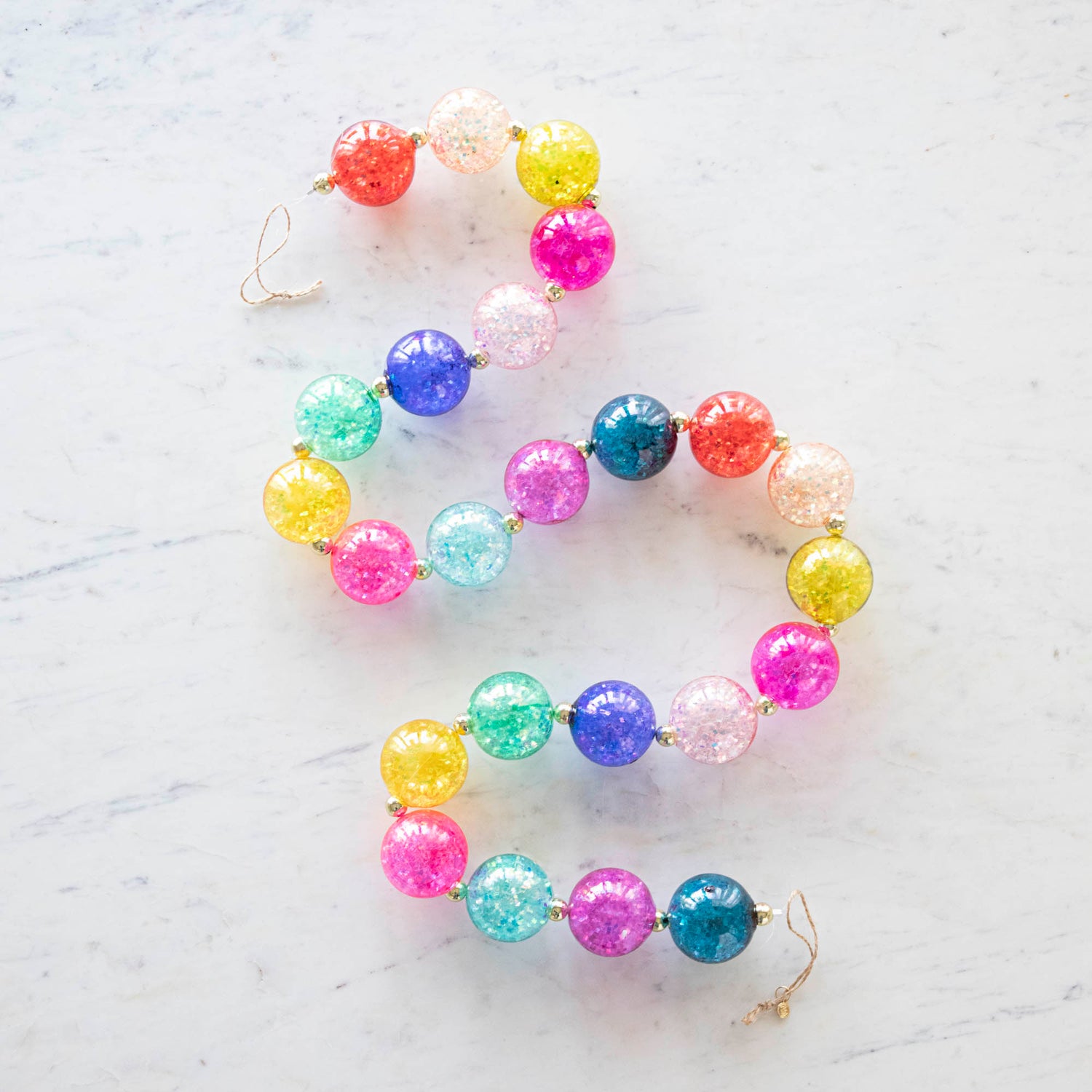 A colorful iridescent ball garland in a s shape, on a marble table.