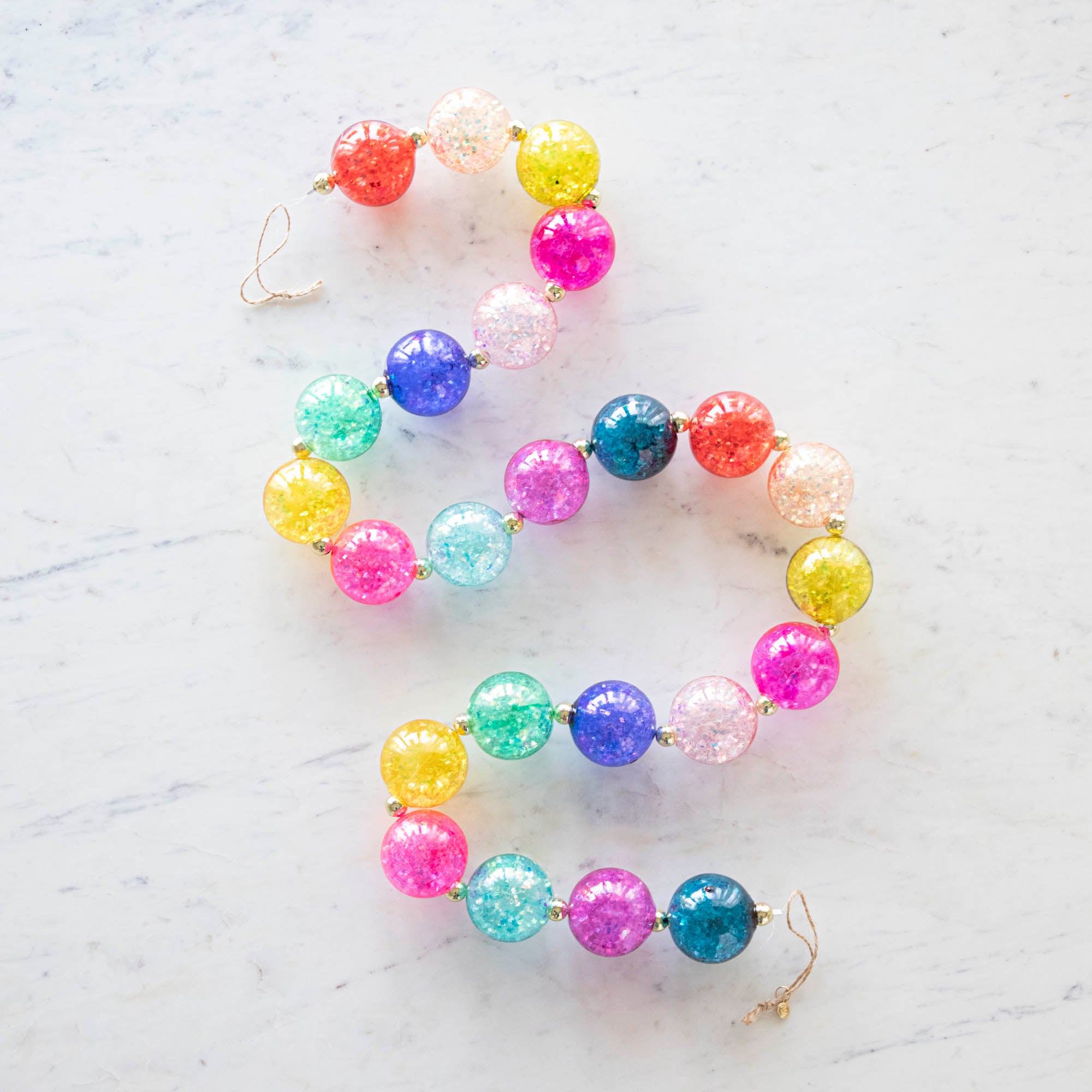 A colorful iridescent ball garland in a s shape, on a marble table.