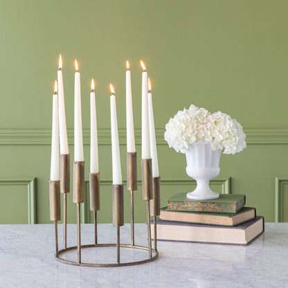 A short, iron taper candle holder with eight lit candles, on a table with flowers stacked on top of various sized books.