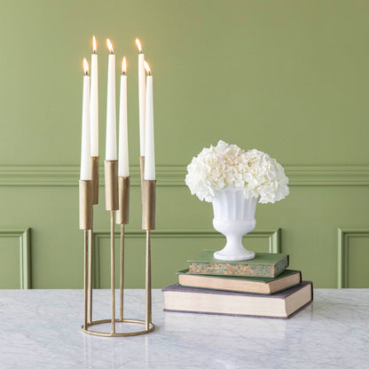 A long, iron taper candle holder with six lit candles in various heights, on a table with flowers stacked on top of various sized books.