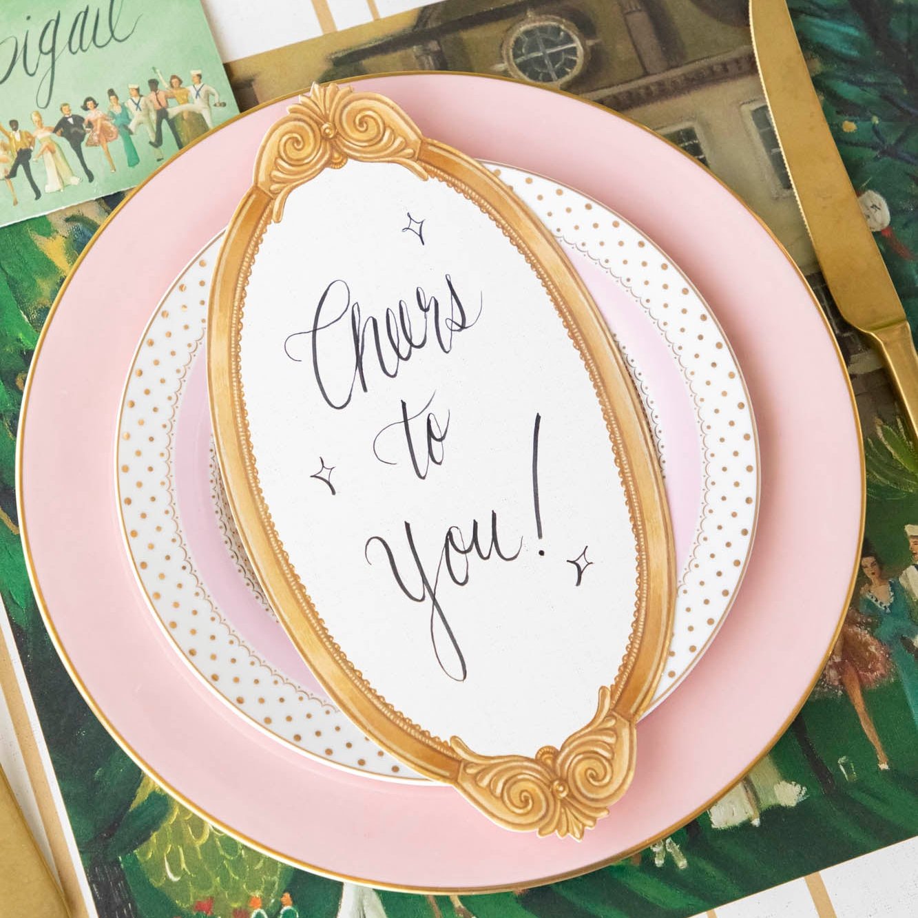 The Antique Gold Frame Table Card with &quot;Cheers to you!&quot; written on it, resting on a dinner plate on an elegant table setting.