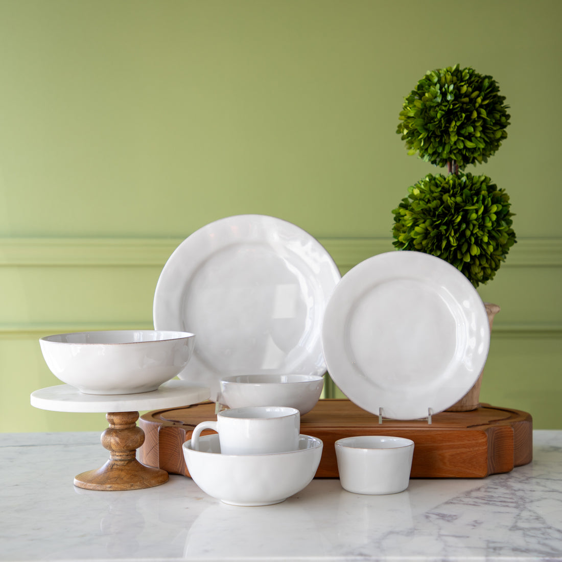 Juliska Puro Whitewash Dinnerware displayed on a table with a topiary plant behind.