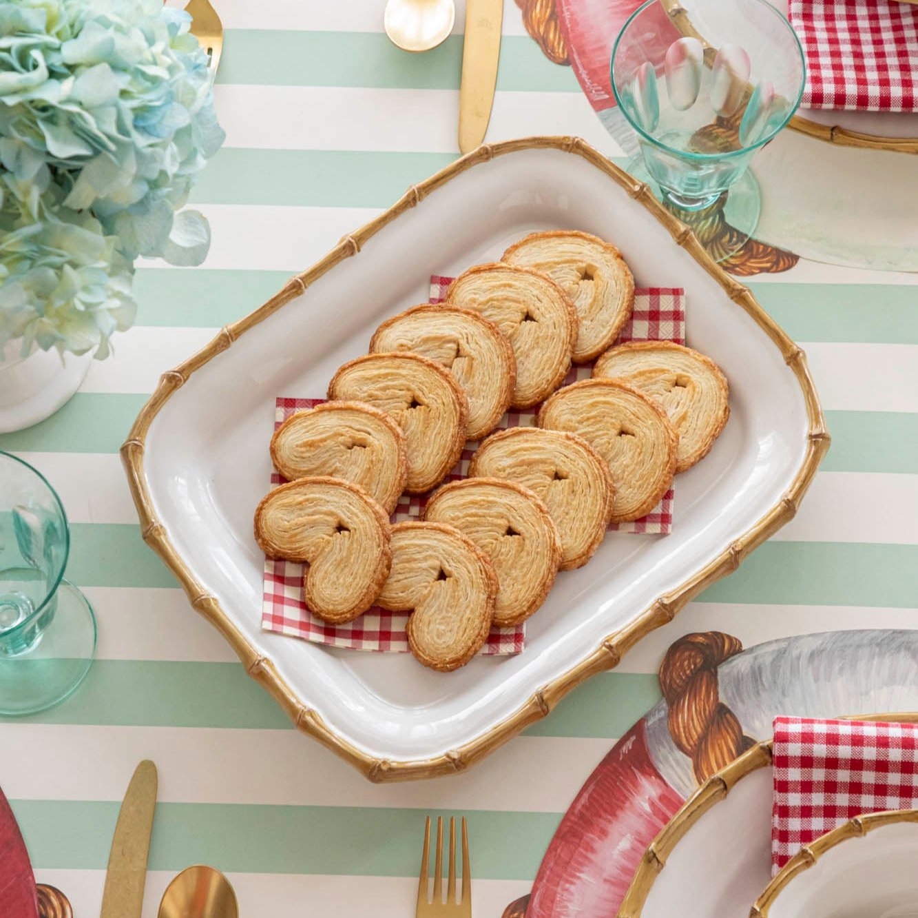 Juliska Bamboo Rectangular server with heart-shaped bread pieces on top of Red Painted Check Napkins, on an elegant table setting.