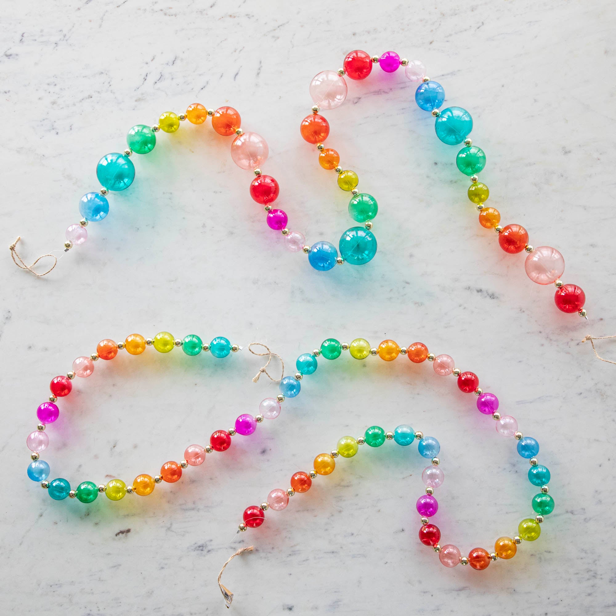 Blown Glass Rainbow Garlands, small and large, on a marble table.