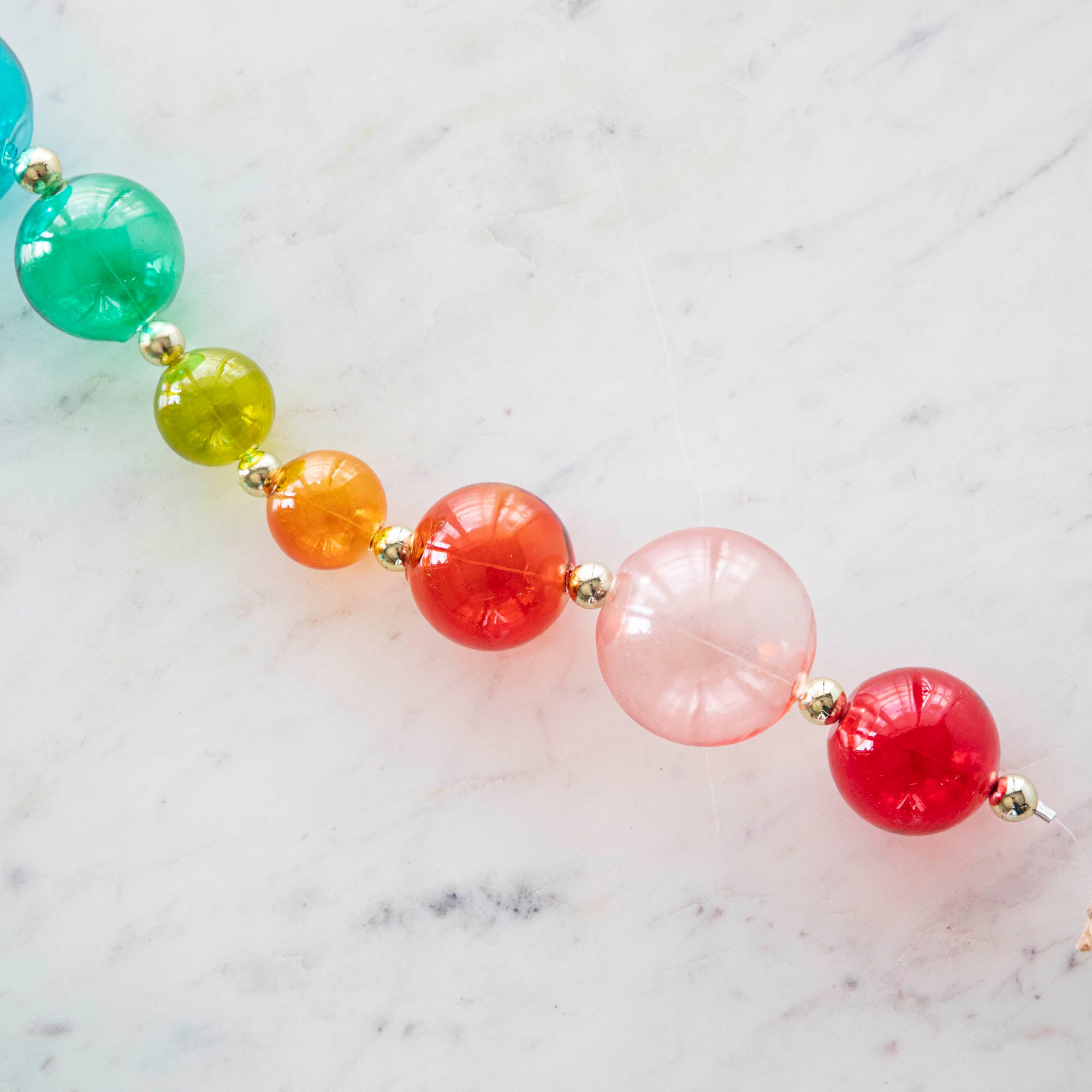 A close up of the colorful Blown Glass Rainbow Garland on a marble table.