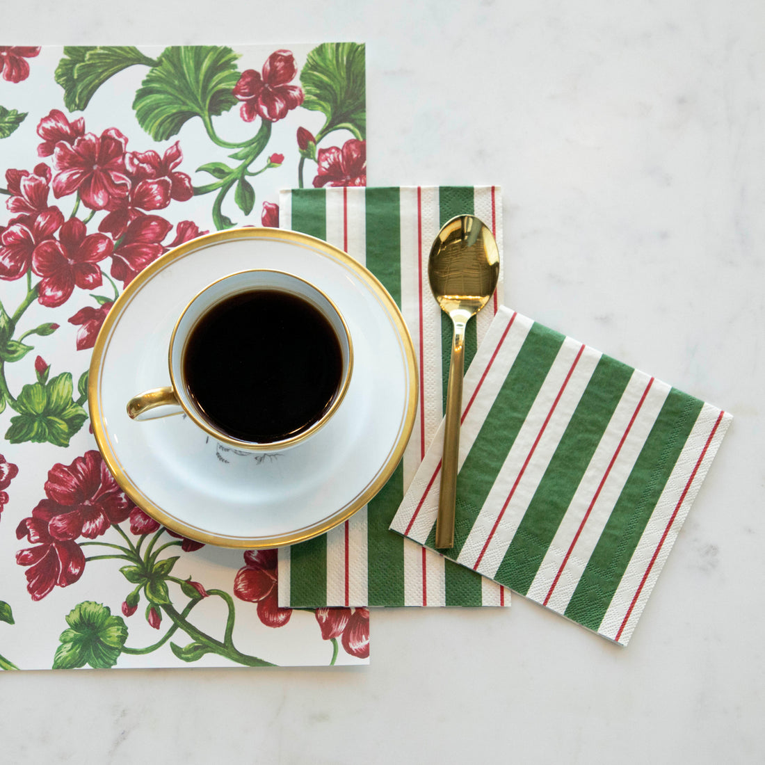 Two Green &amp; Red Awning Stripe Napkins, one Guest and one Cocktail, tucked under a saucer with a cup of coffee on a red and green placemat on a white table, from above.