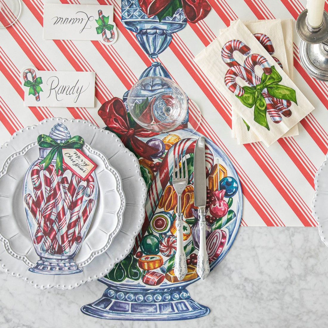 A table setting with the Die-cut Candy Jar Placemat on the Candy Stripe Runner, with white dinner plates and a Candy Cane Jar Table Accent resting on top.