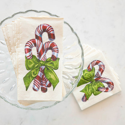 A stack of Candy Cane Guest Napkins fanned out on a glass cake stand, next to a stack of Candy Cane Cocktail Napkins fanned out on the table.