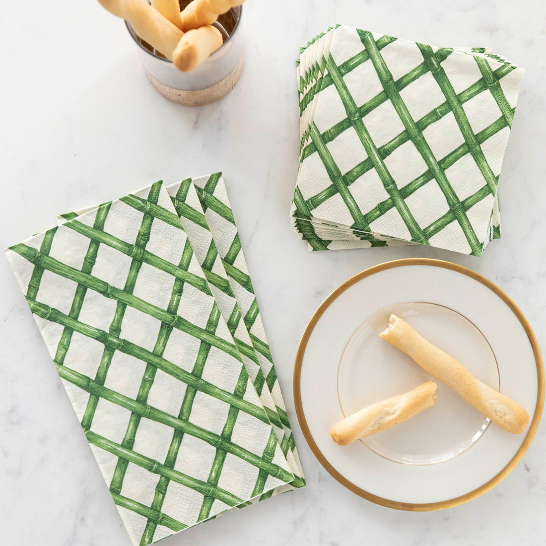 Green Lattice Napkins on a marble table next to small breadsticks on a plate and in a cup.