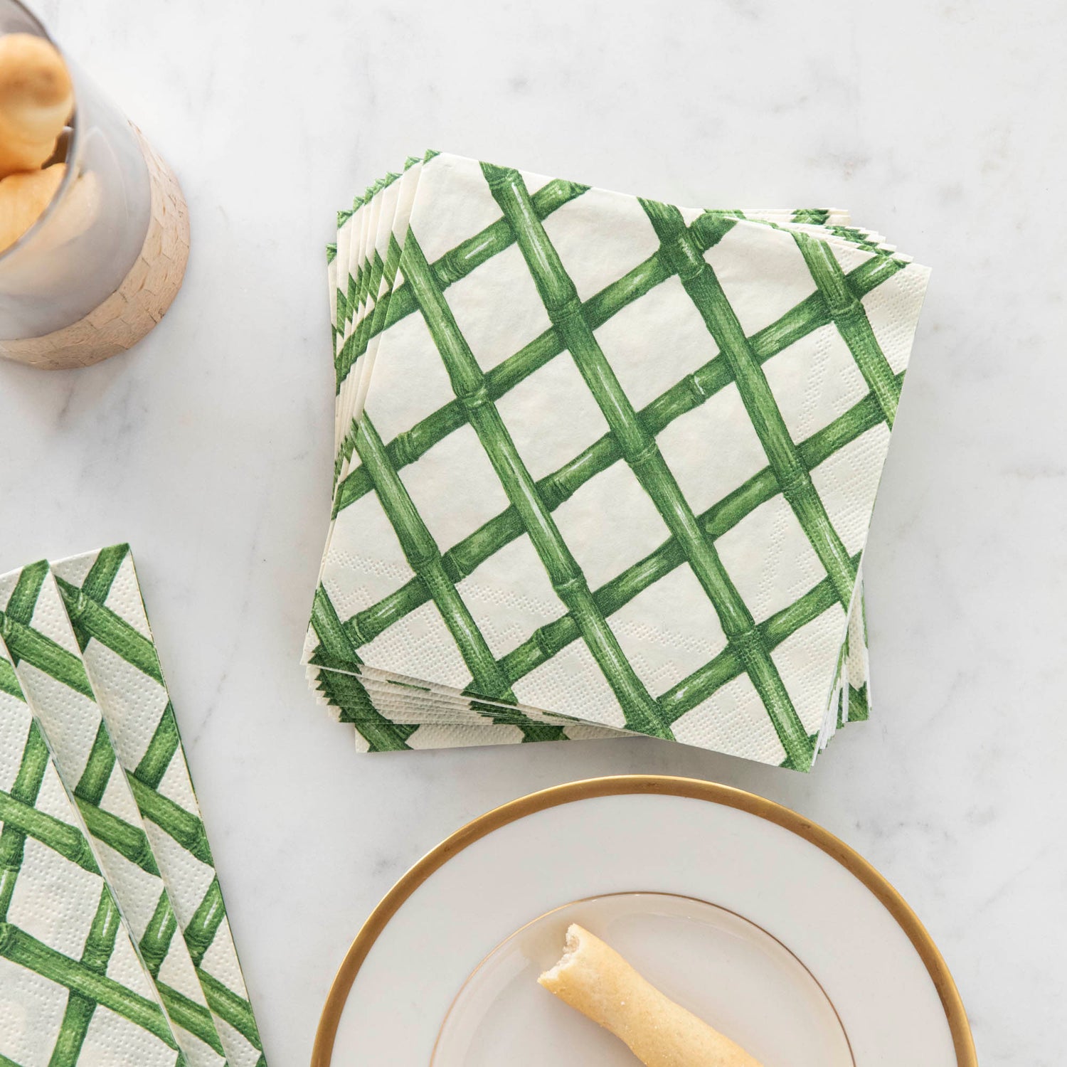 A stack of Green Lattice Cocktail napkins on a marble table next to snacks.