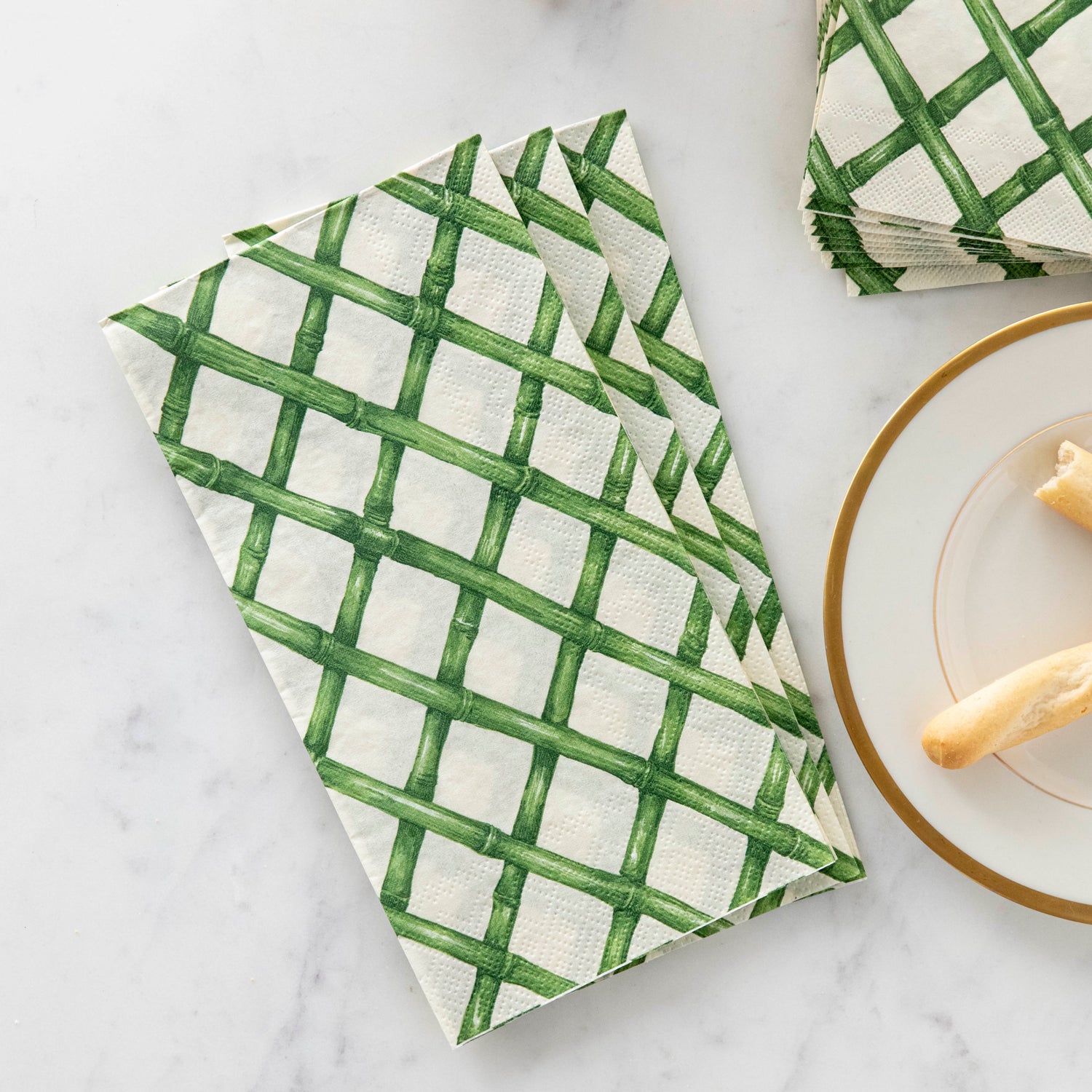 A stack of Green Lattice Guest napkins on a marble table next to snacks.