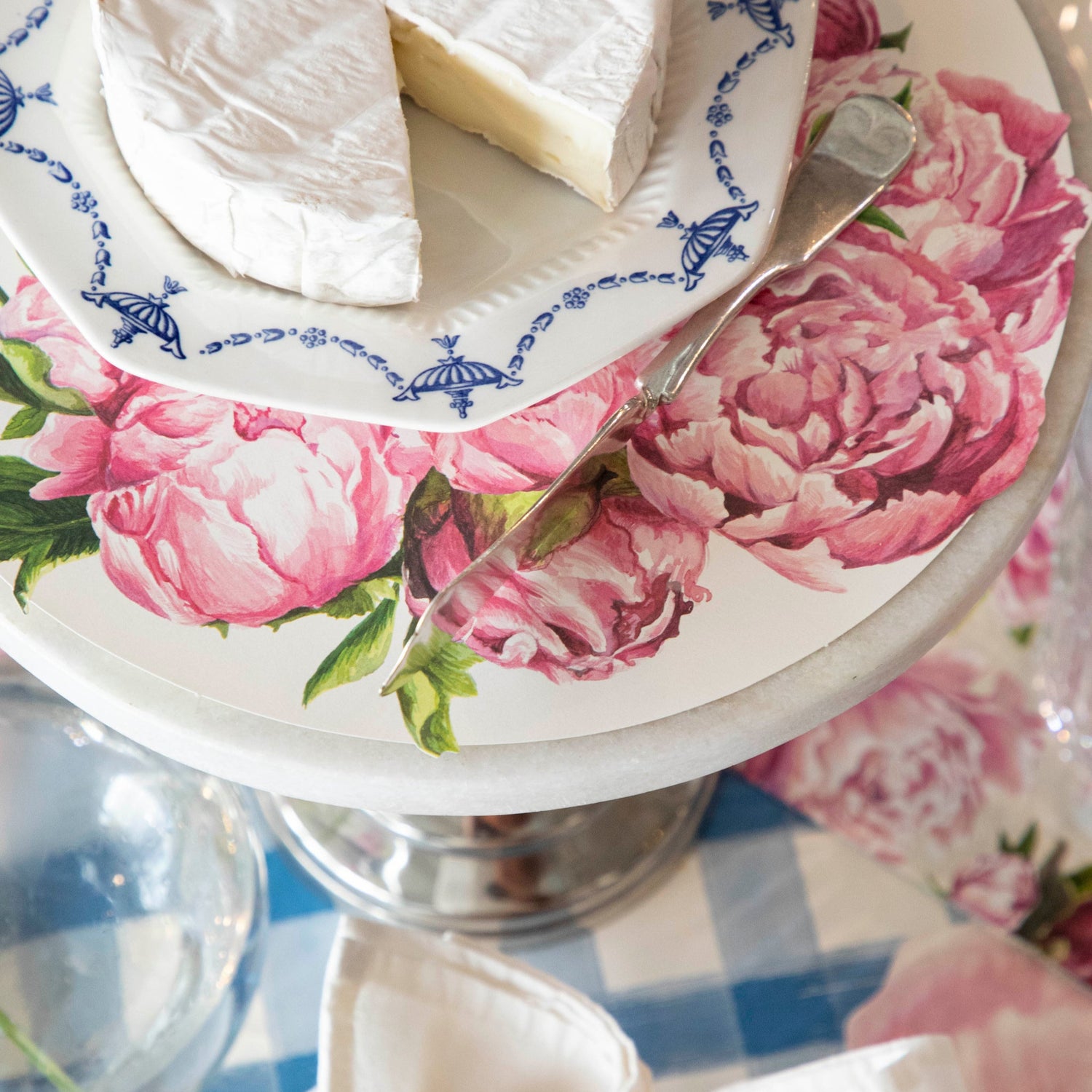 Peony Serving Paper on a cake stand under a plate of cheese, on an elegant table setting.