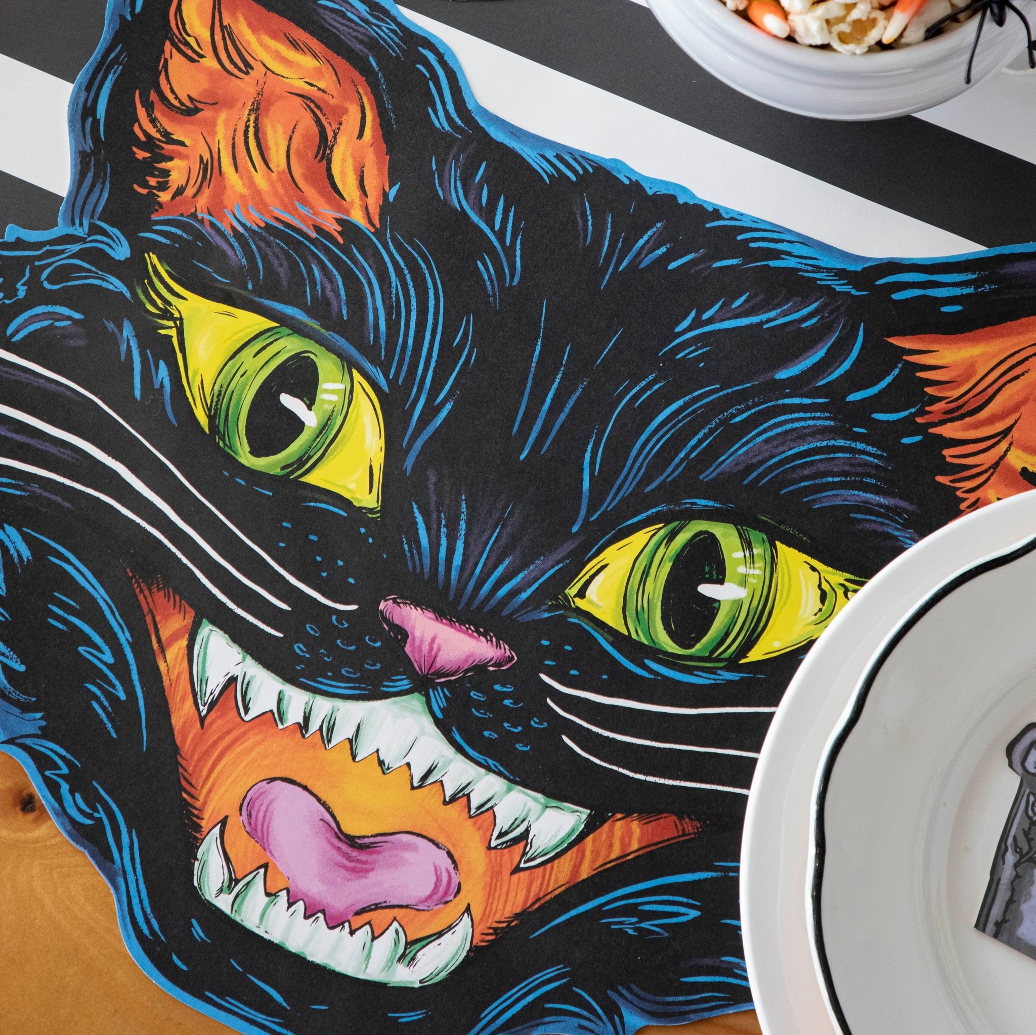 A close up view of the Die-cut Black Cat Placemat featuring blue linework, green and yellow eyes and orange details.