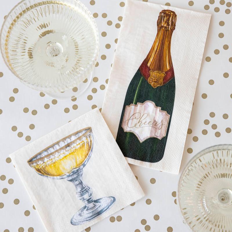 A top-down view of a table with two glasses of champagne with a Champagne Coupe Guest and Cocktail Napkin.