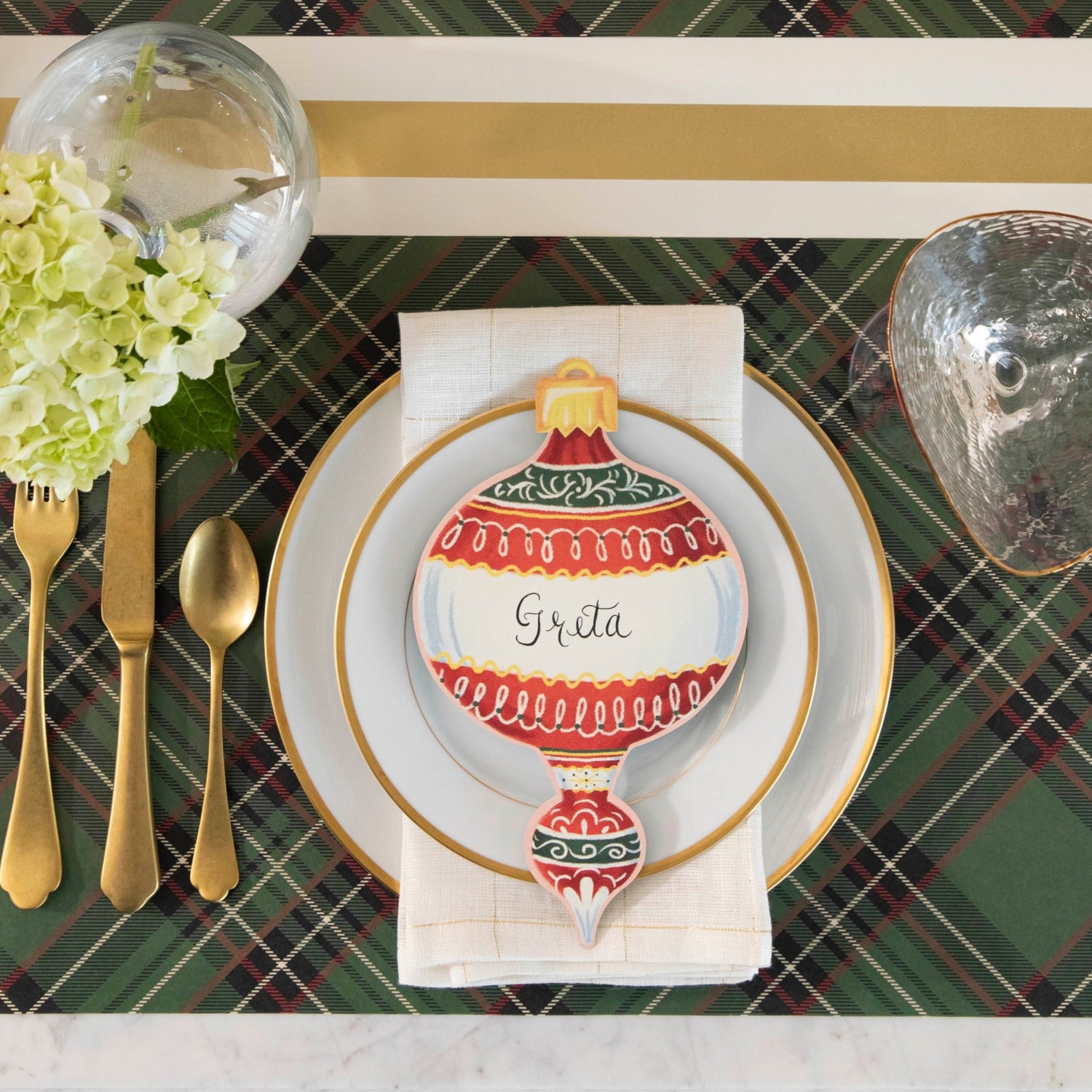 A top-down view of an elegant Christmas place setting featuring an Ornament Table Accent labeled &quot;Greta&quot; resting on the plate.