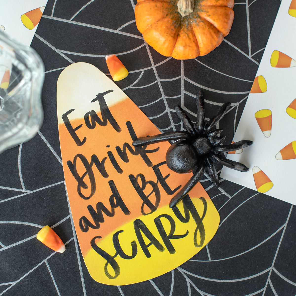 Close-up of a Candy Corn Table Accent resting on a spooky table setting, with &quot;Eat Drink and Be Scary&quot; written on it.