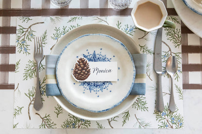 Elegant table setting with the Juniper Sprigs Placemat, a napkin in between two plates and a Pinecone Place Card with the name &quot;Monica&quot; written on it, on top.