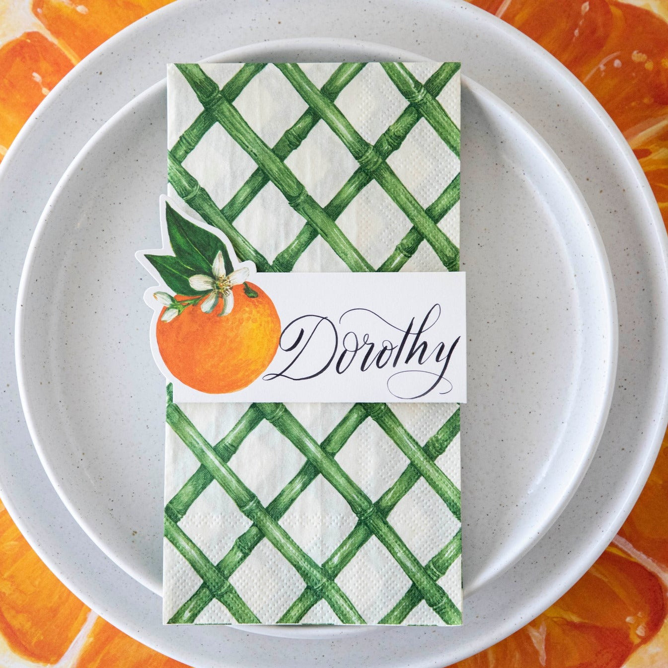 Top-down view of an  citrus-themed place setting featuring an Orange Orchard Place Card labeled &quot;Dorothy&quot; laying flat on the plate.