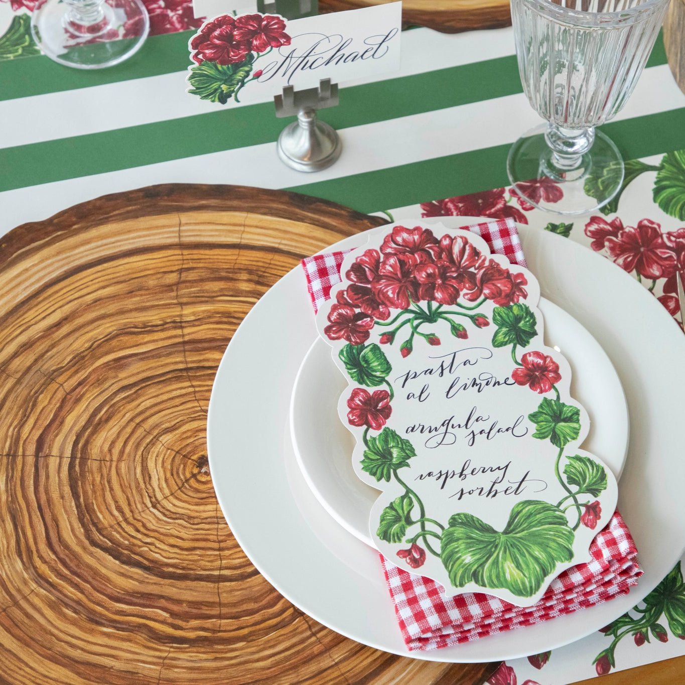 An elegant table setting with a Die-cut Wood Slice Placemat, white plates and a red checkered napkin on top and various Geranium table settings.