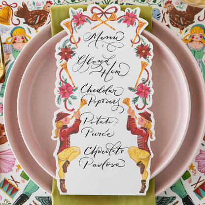 Close-up of a Pipers Piping Table card with a menu written on it resting on the plate of a holiday place setting.