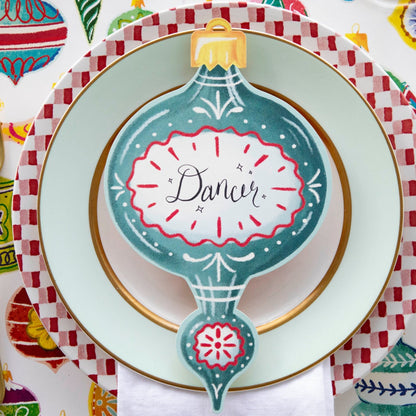 A blue Ornaments Table Accent labeled &quot;Dancer&quot; resting on the plate of a Christmas-themed place setting, from above.