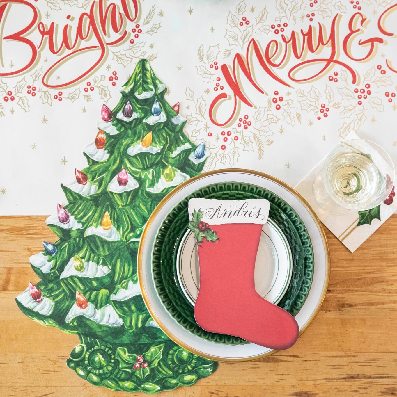 The Stocking Table Accent with &quot;Andres&quot; written on it, resting on a plate, on a Christmas themed table setting.