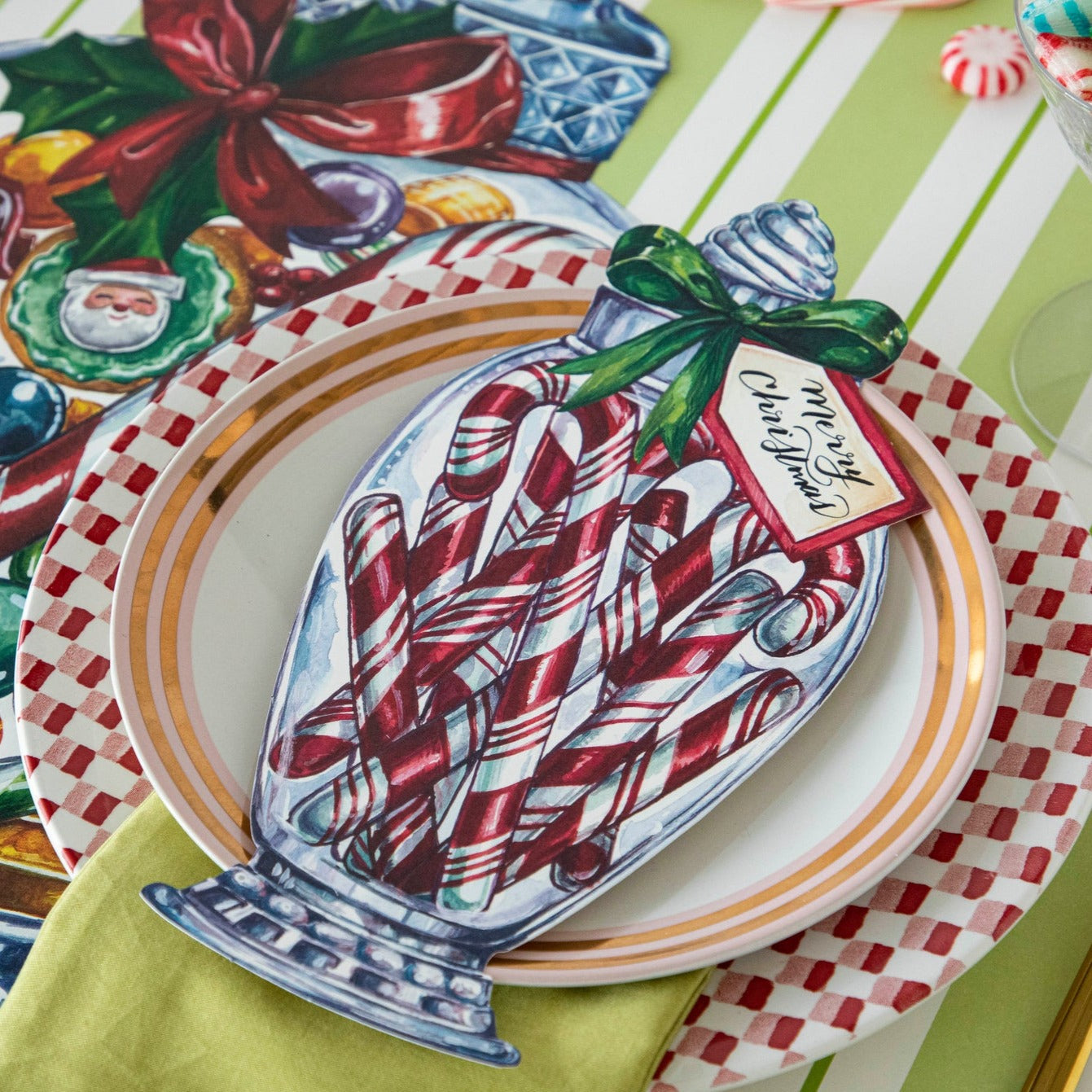 A festive Christmas place setting featuring a Candy Cane Jar Table Accent with &quot;Merry Christmas&quot; written on the tag resting on the plate.