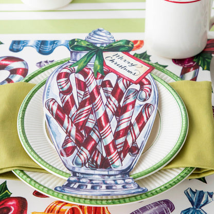 A festive Christmas place setting featuring a Candy Cane Jar Table Accent with &quot;Merry Christmas&quot; written on the tag resting on the plate.