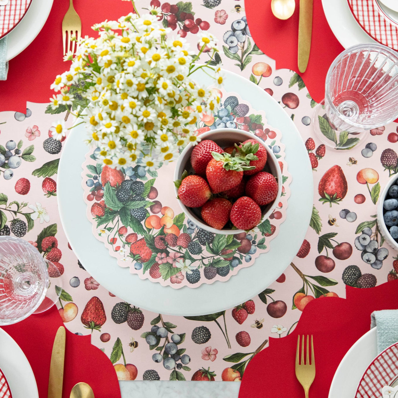 Wild Berry Serving Paper on a cake stand beneath a cup of strawberries and a vase of flowers.