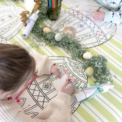 A kid writing her name on the Greenhouse Hare Place Card with the Die-cut Coloring Easter Egg Placemat.