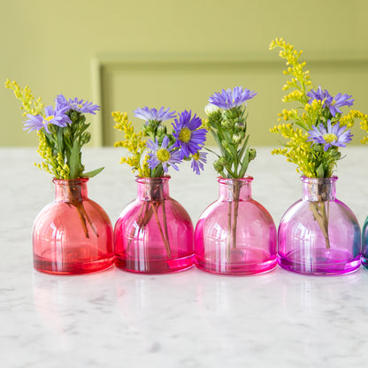 Four round Jewel Tone Glass Bud Vases in red to  purple colors with flowers in them.