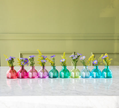 Round Jewel Tone Glass Bud Vases in ranging from red to blue, with flowers in them.