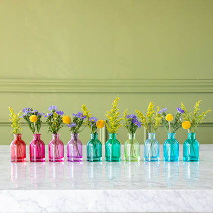 Tall Jewel Tone Glass Bud Vases ranging from red to blue, with flowers in them.