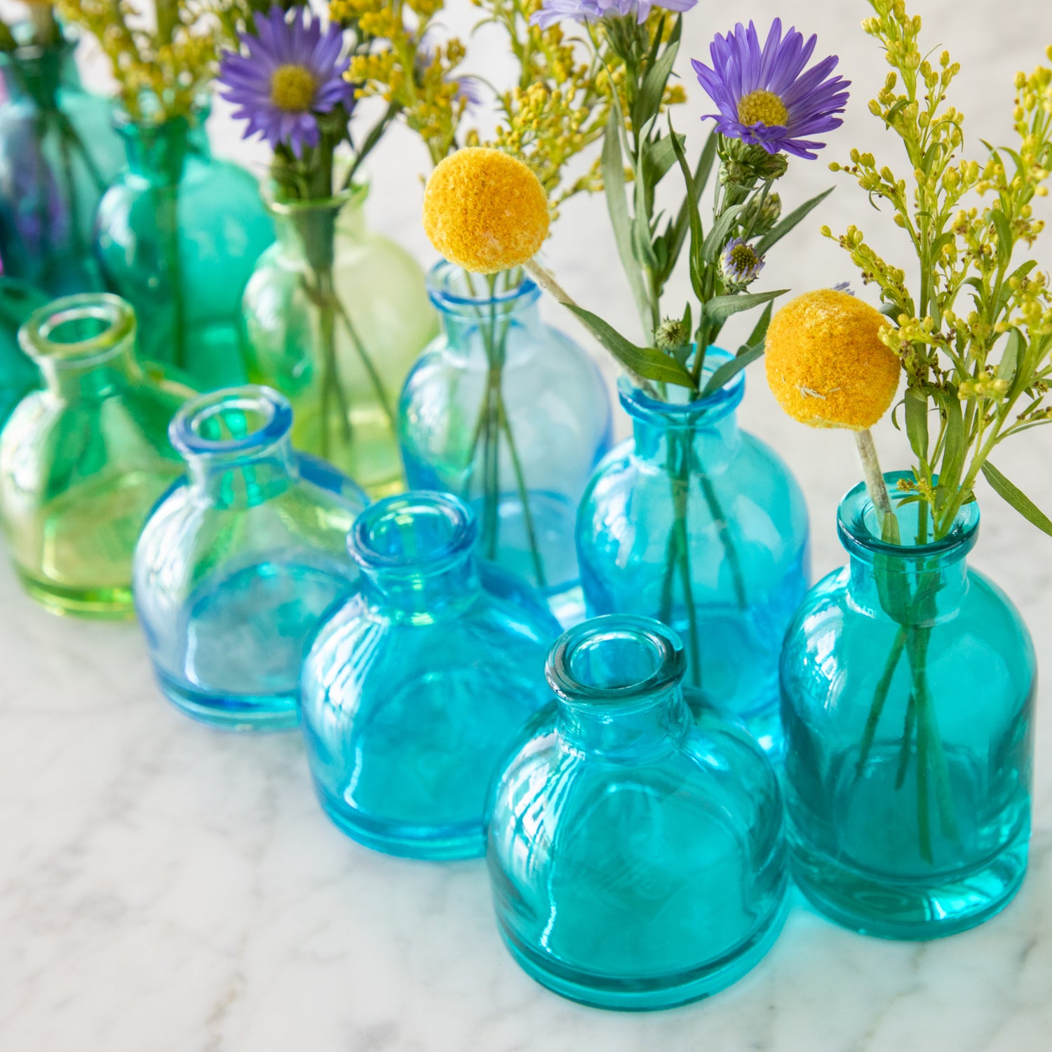 Tall and round Jewel Tone Glass Bud Vases ranging from colors green to blue.