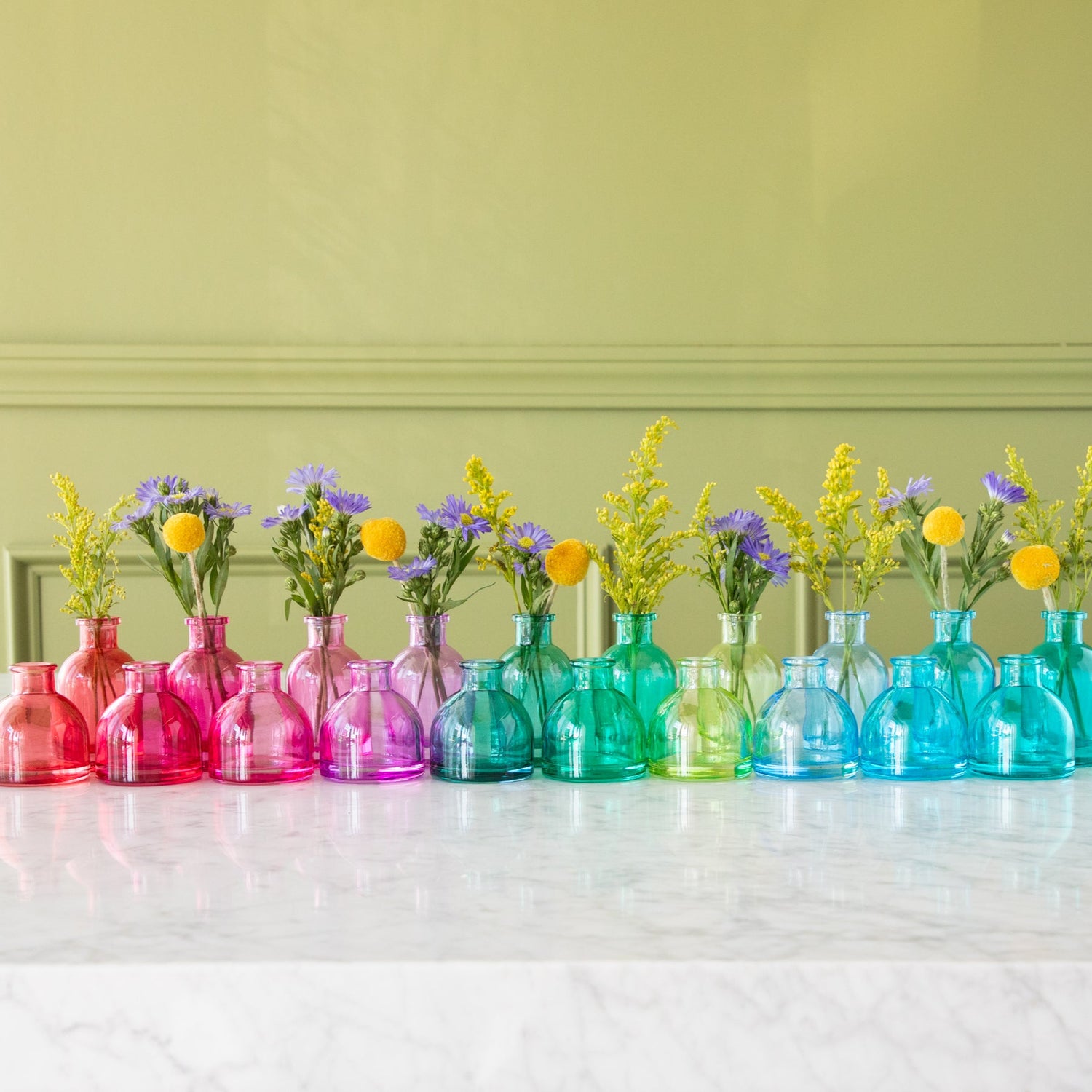 Assorted Jewel Tone Glass Tall Bud Vases with flowers in them, behind the round jewel tone glass bud vases.