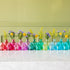 Assorted Jewel Tone Glass Tall Bud Vases with flowers in them, behind the round jewel tone glass bud vases.