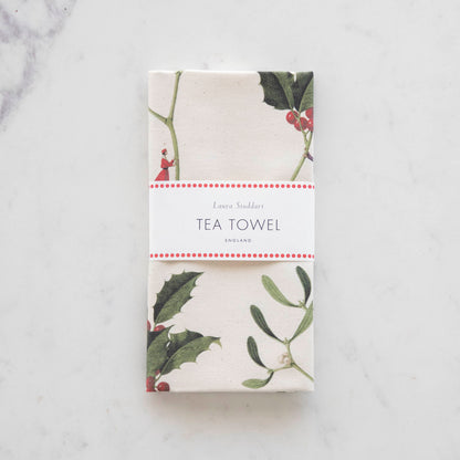 The Laura Stoddart Holly &amp; Mistletoe Tea Towel folded with a white band, trimmed with red dots around it, and the words &quot;Laura Stoddart&quot;, &quot;Tea Towel&quot; and &quot;England&quot; on it.