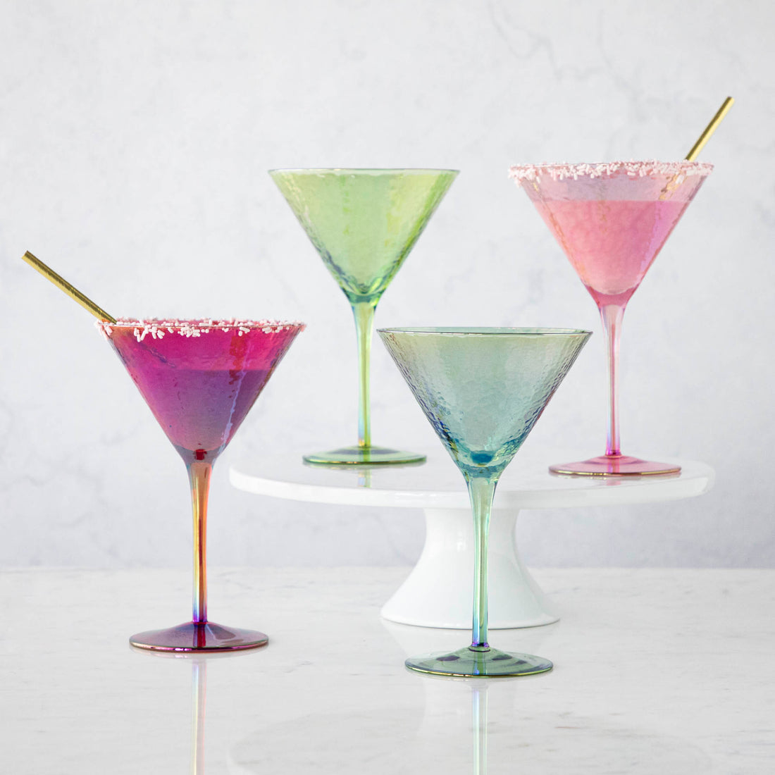 Four stylish Luster Aperitivo Martini Glasses in Zodax with sugar rims on a white stand against a marble background.