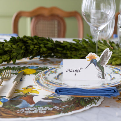 Hummingbird Place Card with Margot written on it, on a garden themed place setting with the Die-cut Songbird Wreath Placemat.