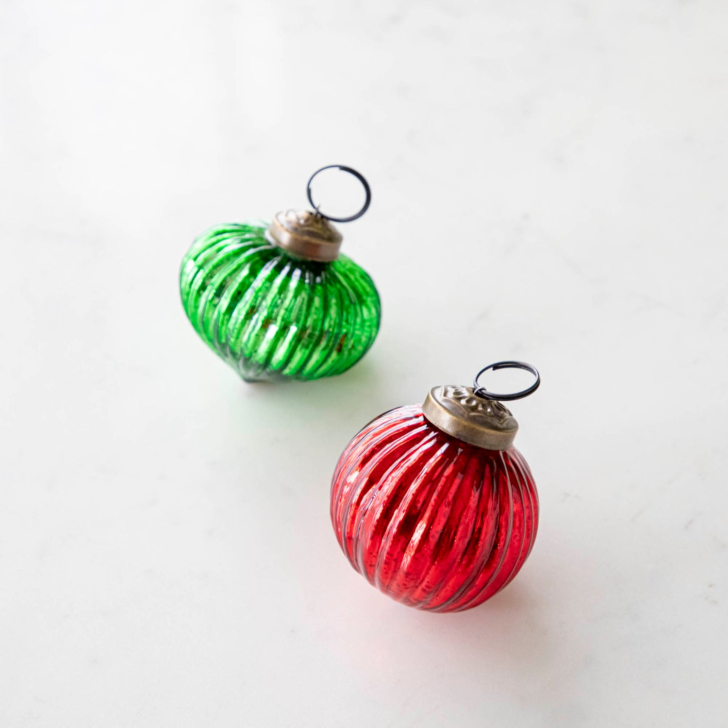 Mini green and red ribbed ornaments on a marble table.