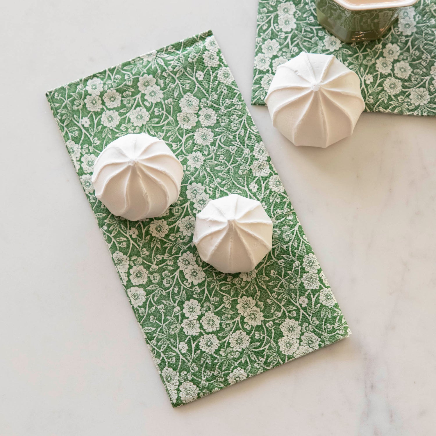 Some marshmallow treats sitting on a Green Calico Guest Napkin, on a white table.