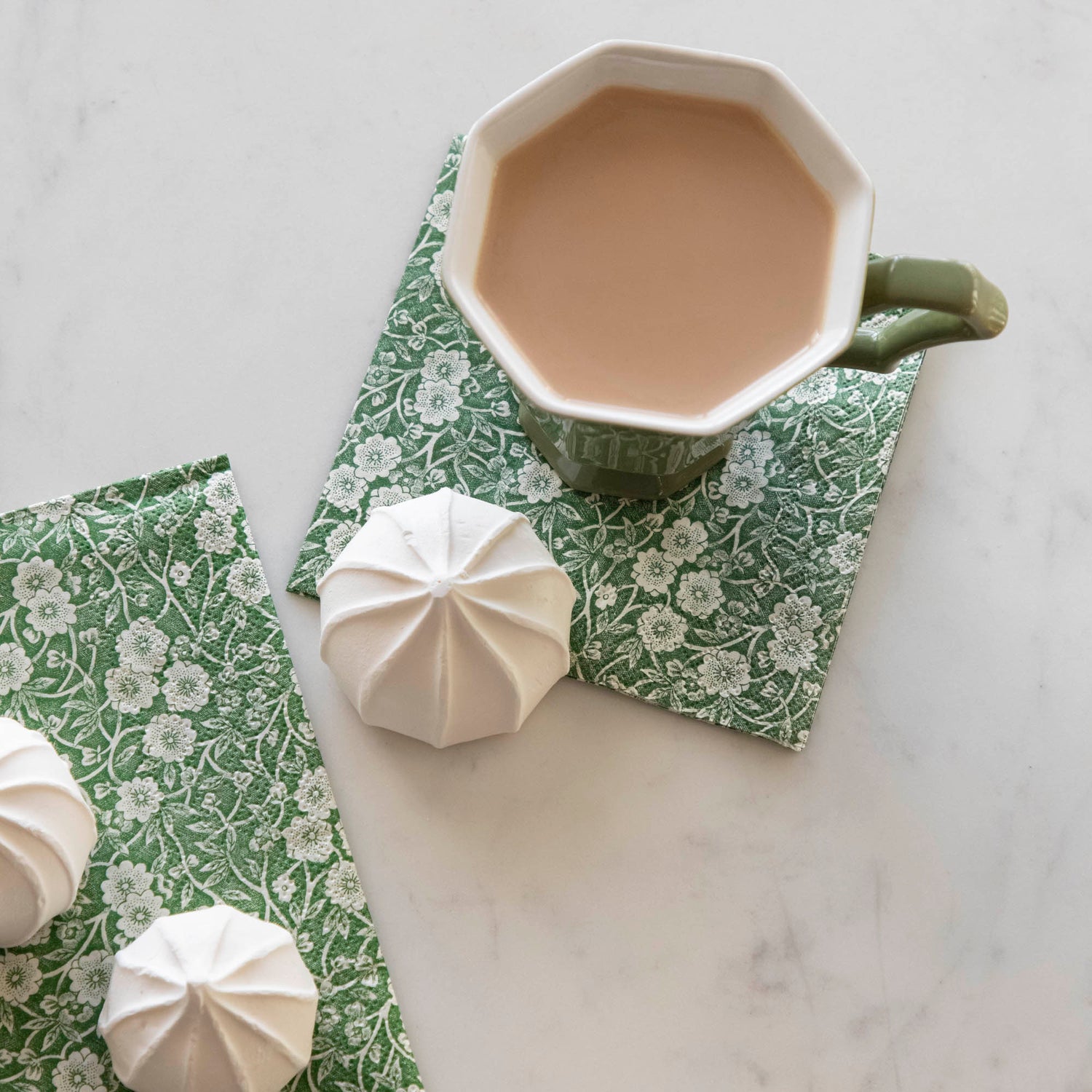 A Green Calico Cocktail Napkin under a cup of coffee on a white table.