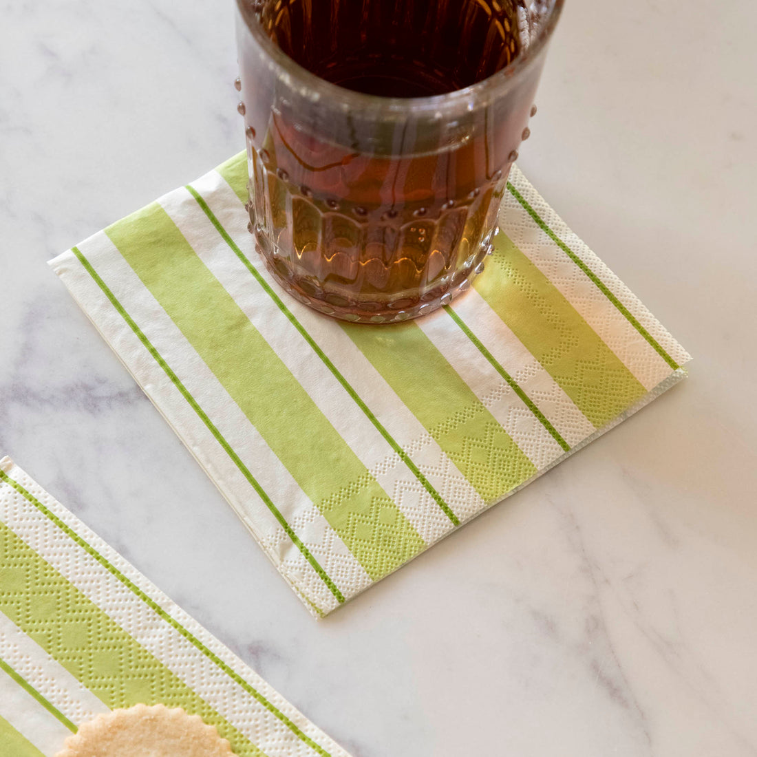 A Green Awning Stripe Cocktail Napkin under a full glass in an elegant place setting.